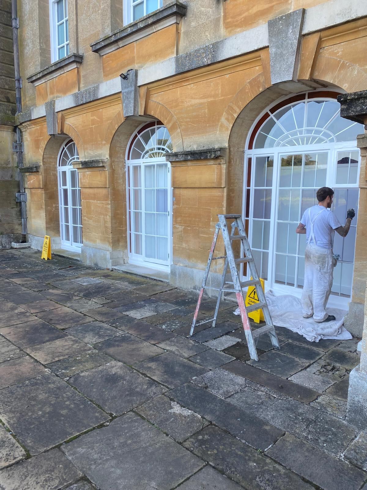 Brierty decorator painting tall arched sash windows on Blenheim Palace exterior, Woodstock Oxfordshire