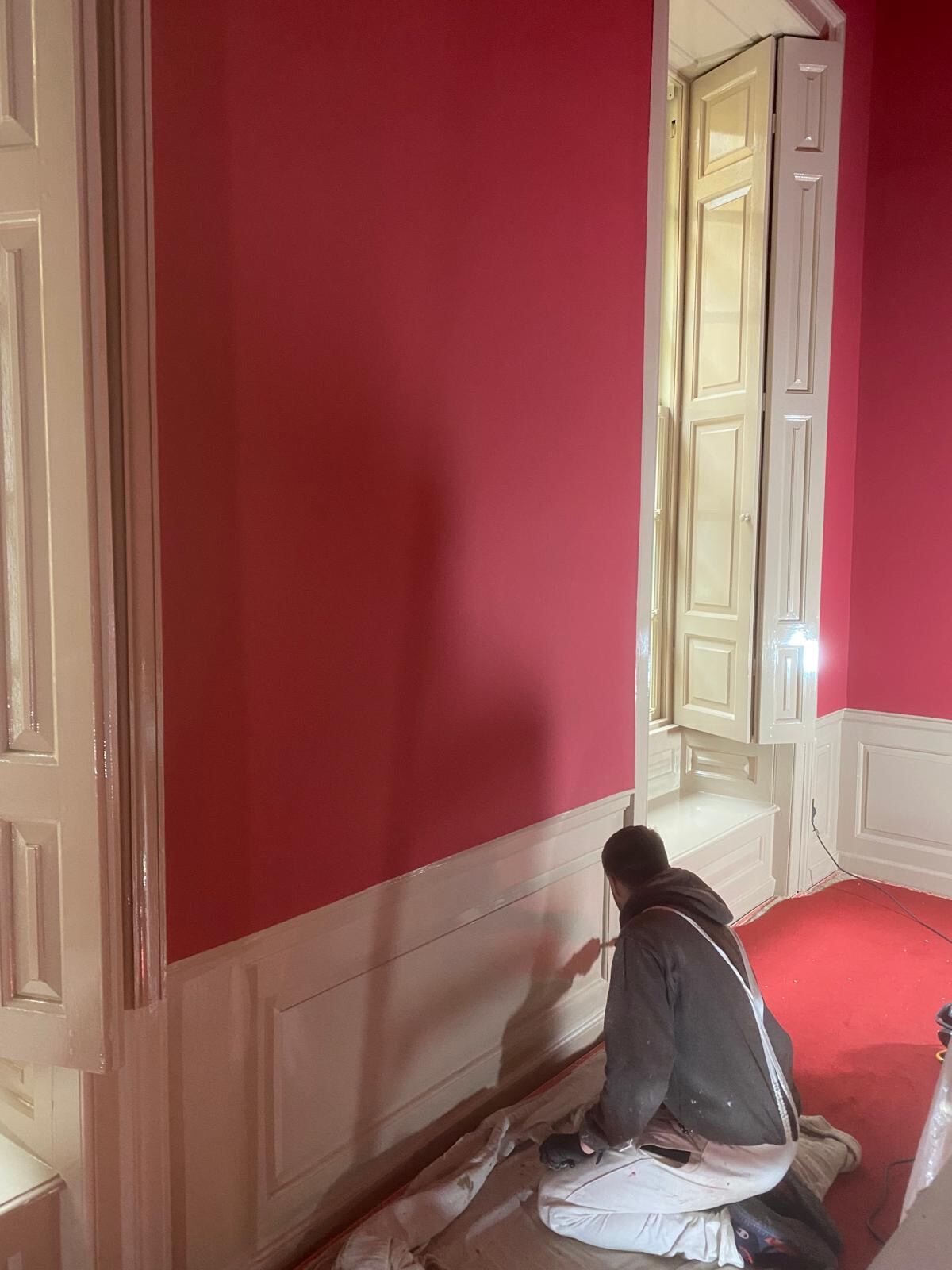 Brierty decorator cutting in white wainscoting against heritage red state room walls at Blenheim Palace